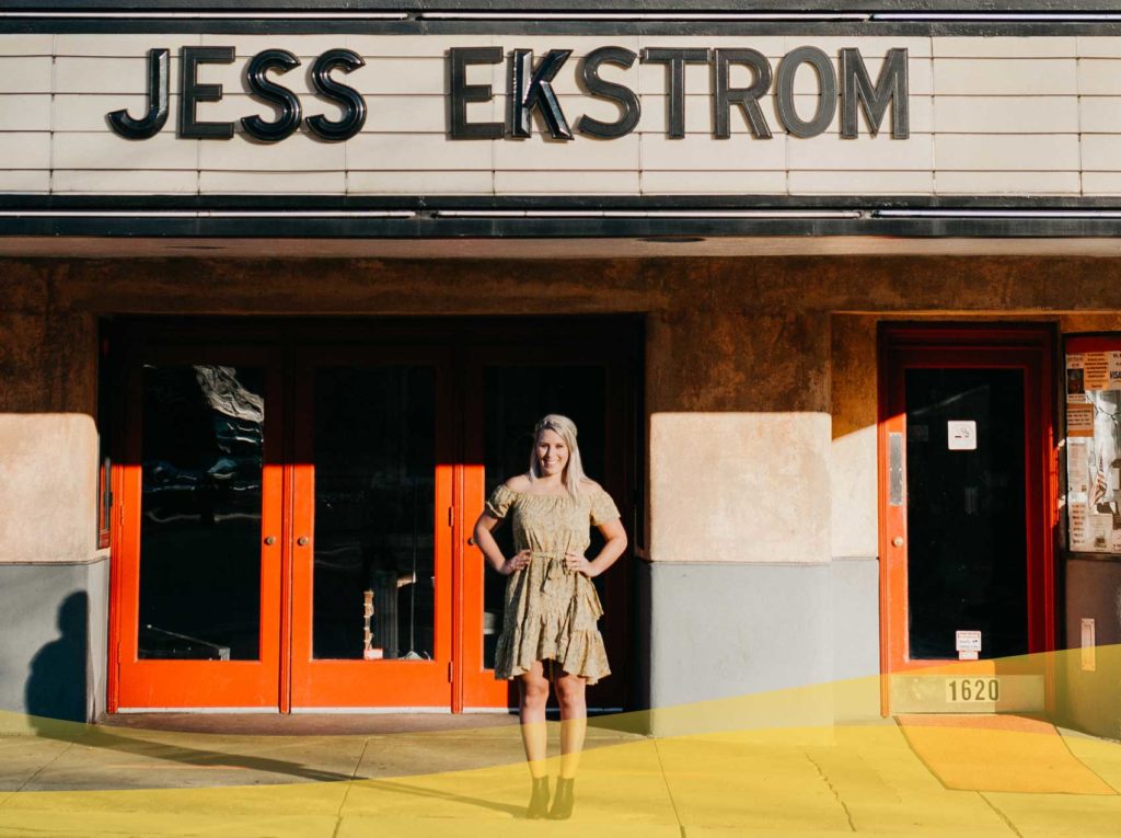Jess Ekstrom standing outside of a building with a sign that has her name in big letters